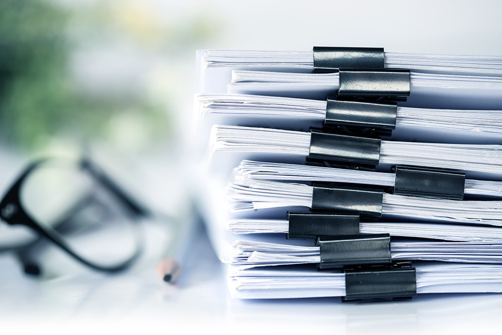 Pile of papers, pencil, and reading glass