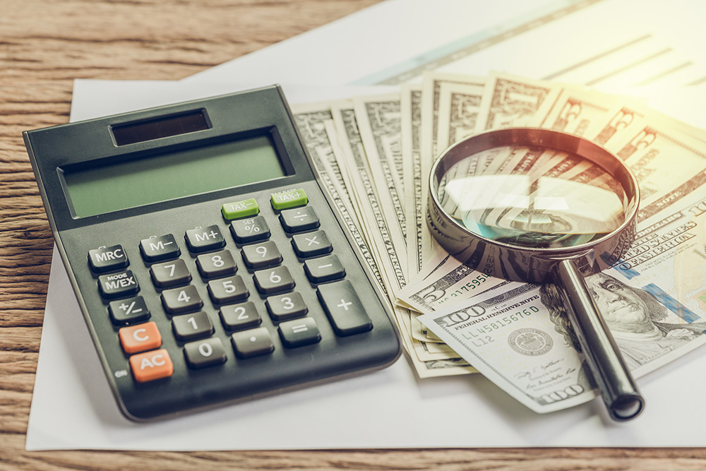 Magnifying glass sitting on dollar bills beside calculator