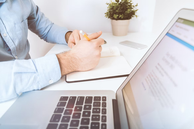 Man writing on a book beside laptop